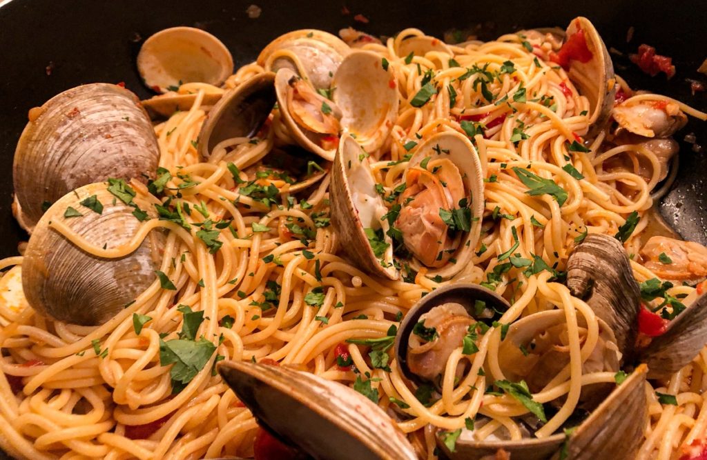 littleneck clams resting on bed of spaghetti in pan