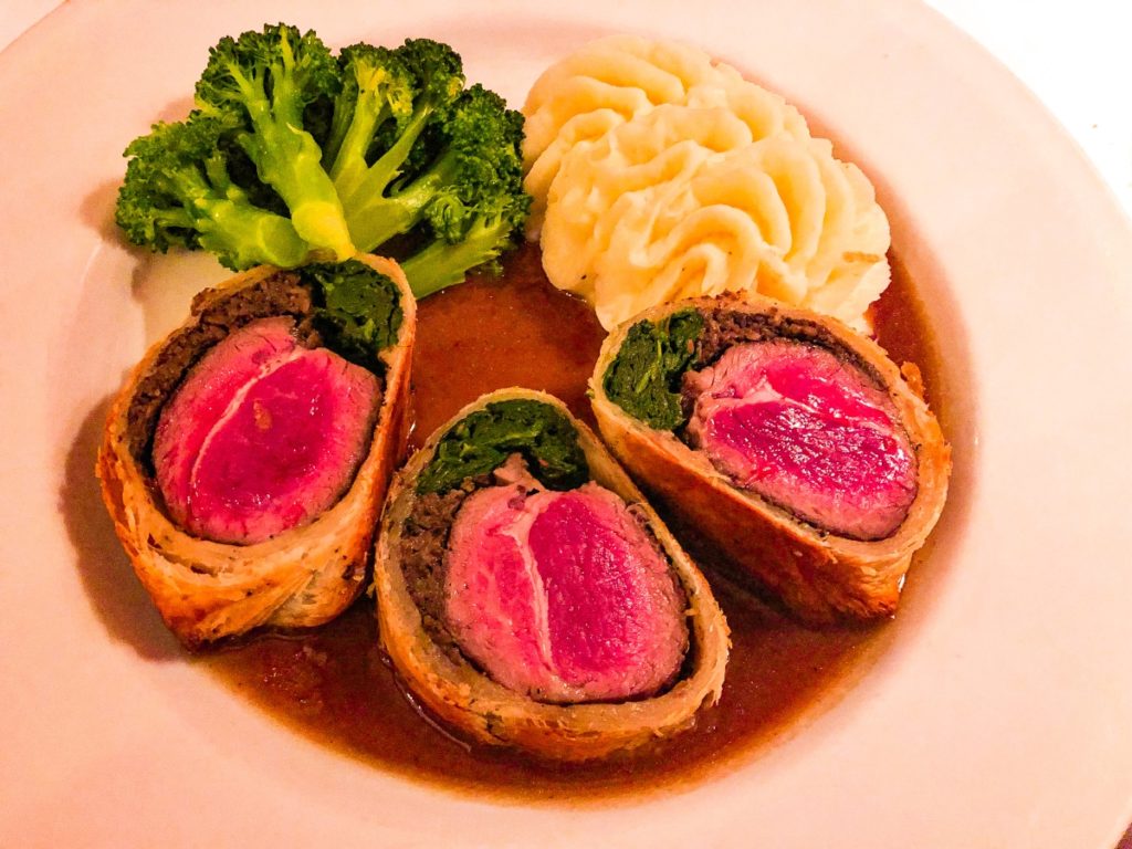 lamb wrapped in puff pastry with mashed potatoes and broccoli on a plate